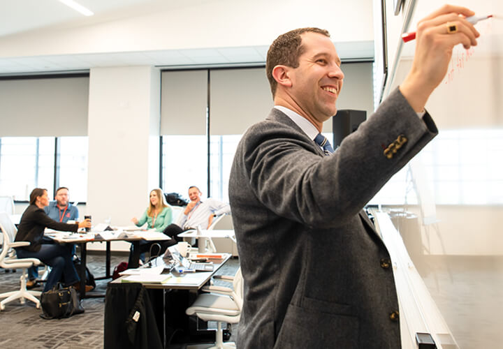 Smiling instructor writes on whiteboard in front of class