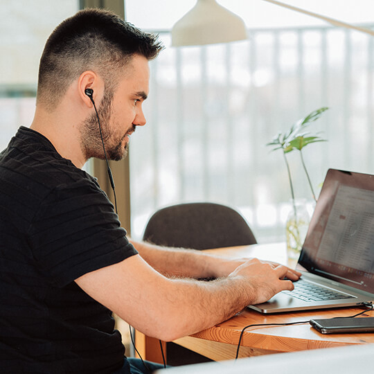 Person wearing ear buds works on a laptop