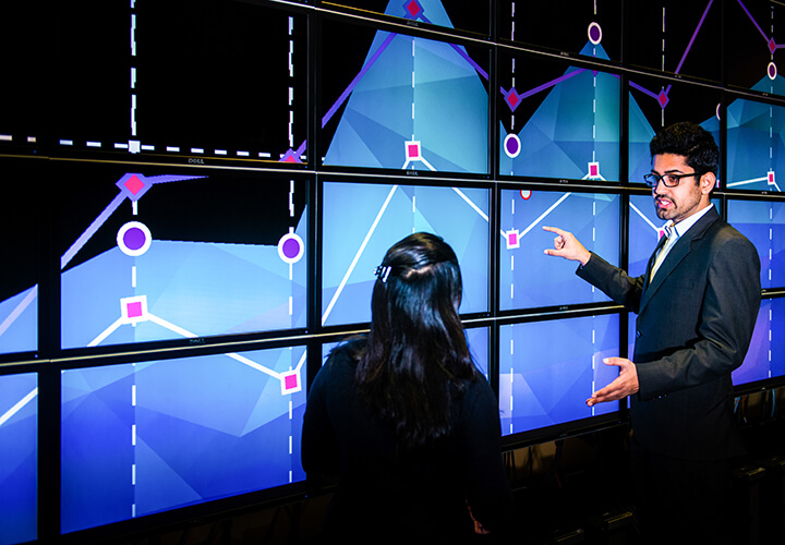 Two people analyze graphs on wall of screens