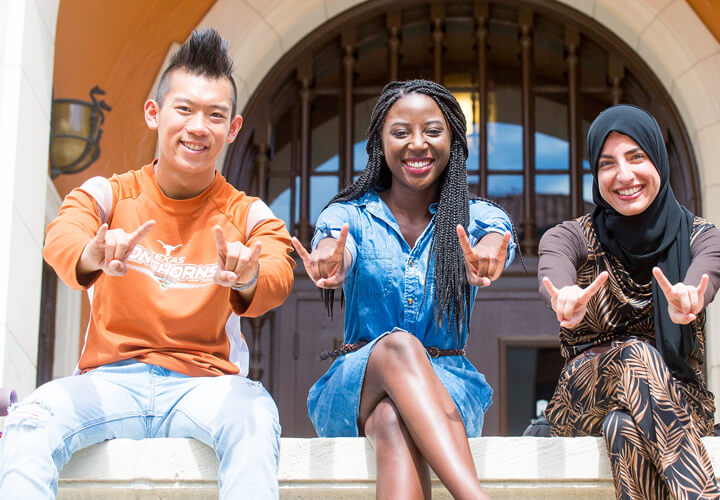 Three students on bench giving hook em horns