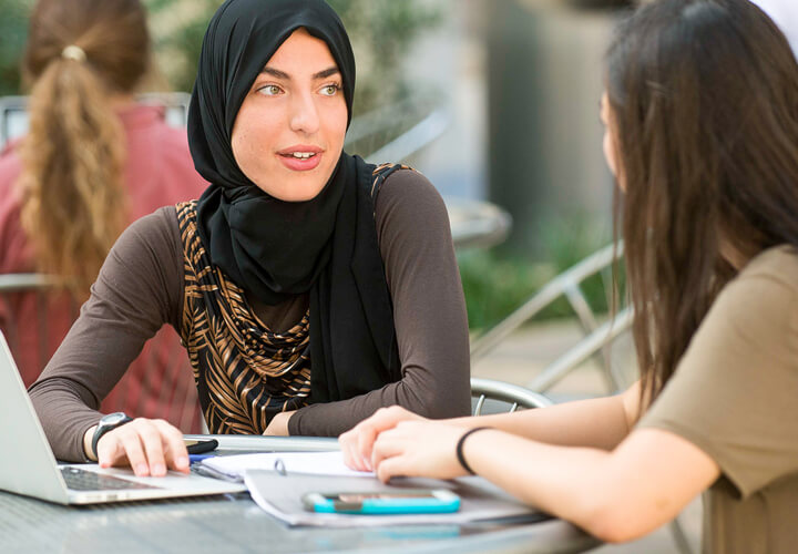 Two students talk together at table