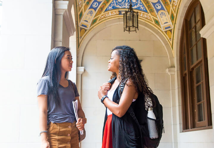 Two students talk under archway on University of Texas campus