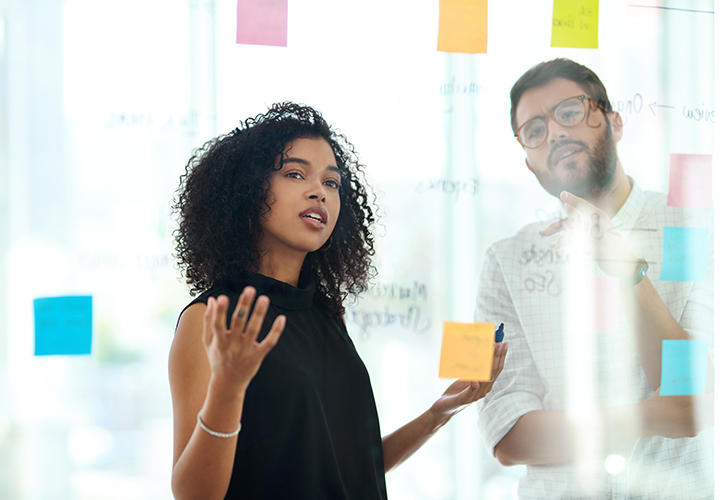 two businesspeople brainstorming with notes on a glass wall in a modern office