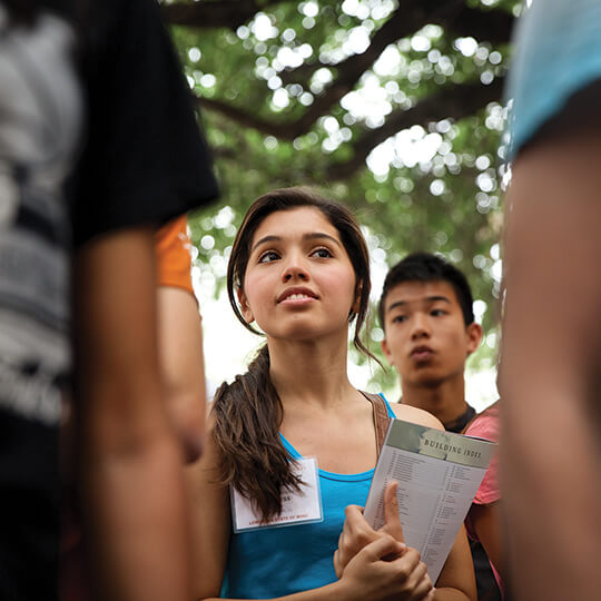 Student holding a booklet in the west mall under trees.