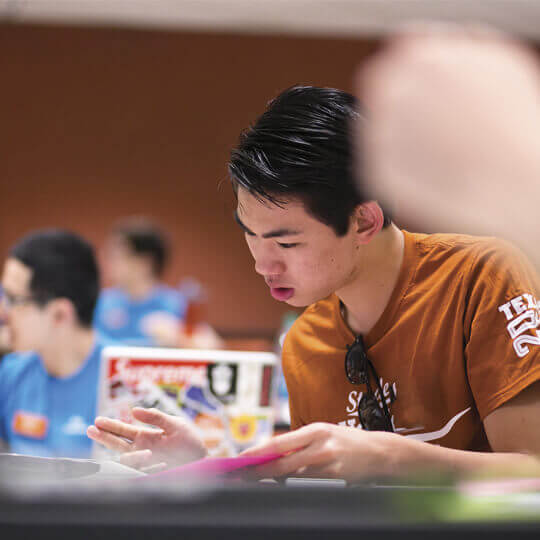 Student sitting in a lecture room in front of a laptop and filling out paperwork.