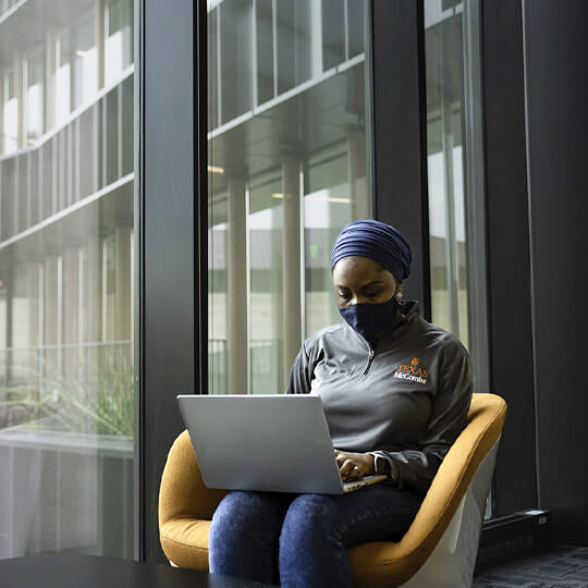 Masked student works on laptop