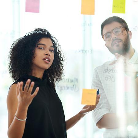 two businesspeople brainstorming with notes on a glass wall in a modern office