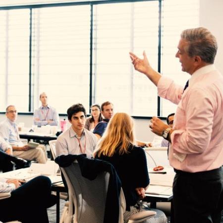 Man stands in front of classroom and explains something with hand up.