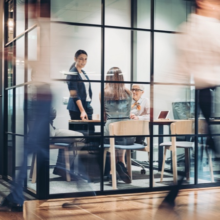 Exterior view of a glass meeting room with people inside of it.