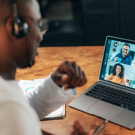 Person sitting at a laptop with headphones on participating in video call.