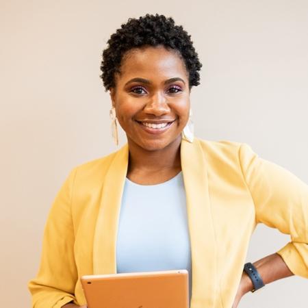 Woman in yellow blazer holding laptop smiling.